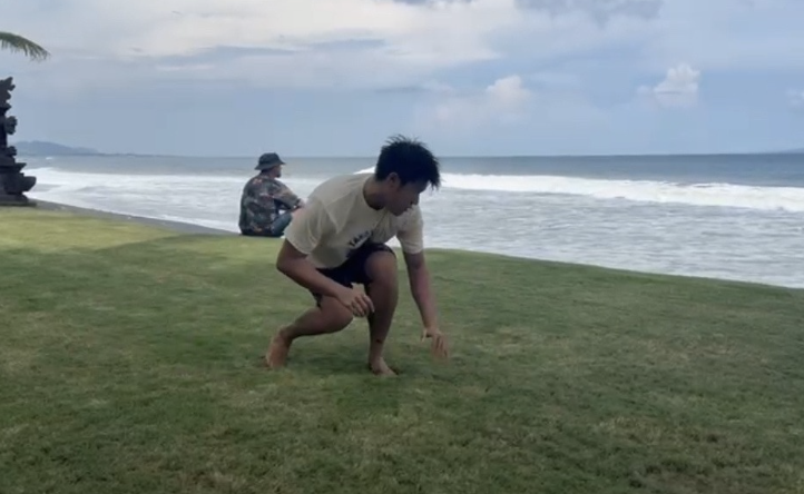 A Freesurf Federation rider practicing a Wave Ki low stance on the grass above the lineup
